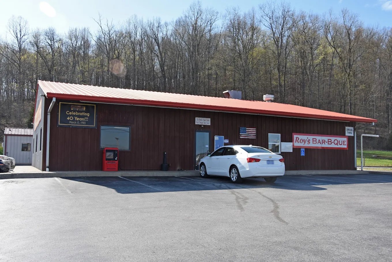 Exterior of Roy's Pit Bar-B-Q, a brown building with a red roof and parking lot